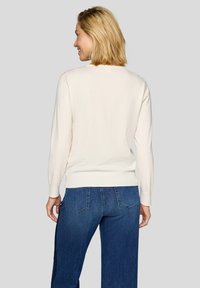 Helles cremefarbenes Sweatshirt aus weichem Strickmaterial, mit rundem Ausschnitt und gerippten Bündchen, kombiniert mit dunkelblauen, weit geschnittenen Jeans.
