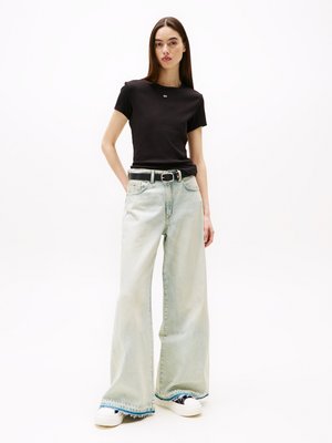 T-shirt noir à manches courtes, jeans bleu clair à jambes larges avec un ourlet effiloché, associé à des baskets noires et blanches. Détail de logo simple sur le t-shirt.