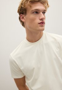Crème kleurig t-shirt met korte mouwen, gemaakt van zachte stof; heeft een ronde halslijn en een lichte glans; gladde textuur zonder patronen.