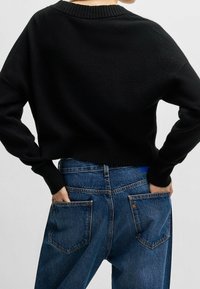 Schwarzer, verkürzter Pullover mit geripptem Kragen und Bündchen, kombiniert mit blauen, hoch taillierten Jeans, die über zwei Gesäßtaschen und ein blaues Etikett verfügen.