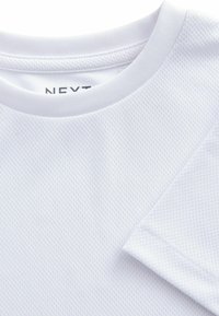 T-shirt de sport blanc en tissu texturé qui évacue l'humidité, avec un col rond et des manches courtes. Étiquette de marque visible à l'intérieur du col.
