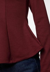 Tuvojoties cilvēkam ar bordo garām piedurknēm un zilu džinsu bikses.