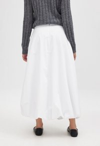 Gonna bianca voluminosa realizzata in materiale leggero, con un design arricciato. Abbinata a un maglione grigio testurizzato e ballerine nere.