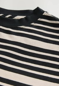 Camiseta de algodón a rayas negras y crema que presenta un cuello redondo, mangas cortas y una textura suave con patrones horizontales uniformes.