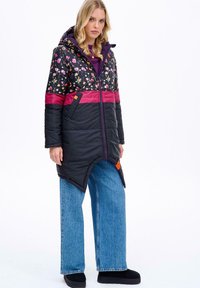 Př padded kabát s květinovým vzorem v černé, fialové a magentové barvě. Má kapuci, zipové uzavírání a asymetrický lem. Nosené s širokými džínami.