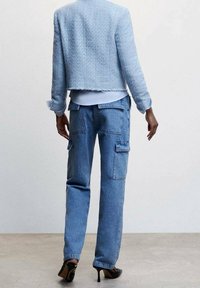 Jasnoniebieska kurtka w tweed z postrzępionym dołem, połączona z jasnoniebieskimi spodniami cargo z denimu, posiadającymi boczne kieszenie i luźny krój. Czarne buty na wysokim obcasie.