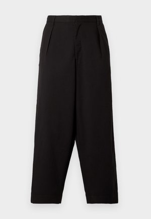 Melni platāki bikses, kas izgatavotas no gludas auduma. Tām ir krokojumi jostasvietā un brīva piegriezuma, beidzoties virs potītes. Nav redzamu metāla detaļu.