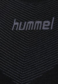 Primer plano de tela negra con el logo de la marca hummel en gris y líneas paralelas diagonales que forman un patrón de chevron.