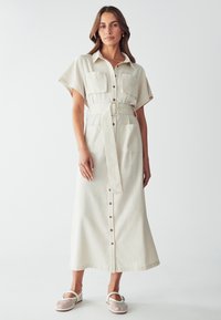 Beige liinapoolne kleit lühikeste varrukatega, nööpide ees, kahe rinna taskuga, vööga talje, sirge lõige ja loomulik tekstuur.