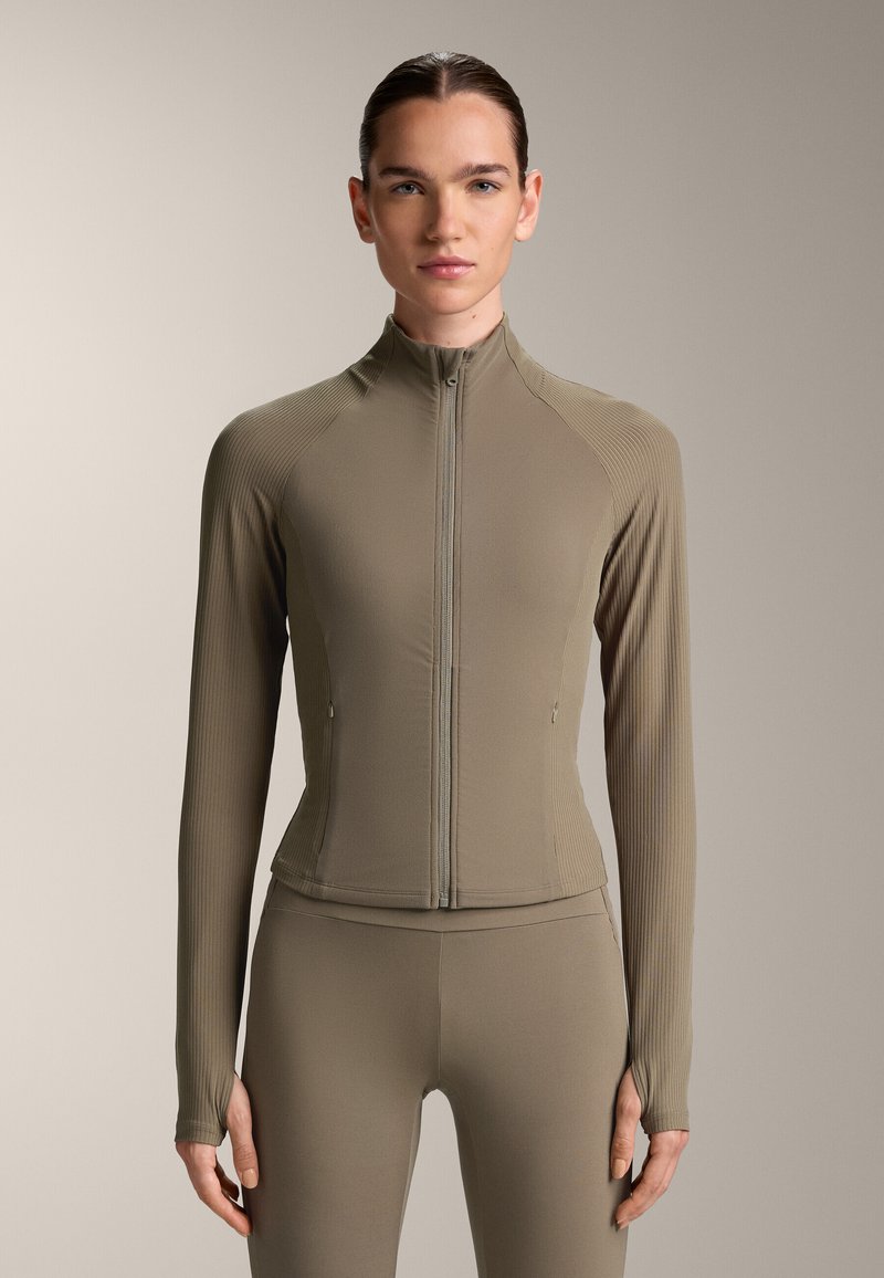 Taupe træningsjakke med en tætsiddende design, ribbet tekstur, høj krave og fuld lynlås. Lange ærmer med tommelhuller, kombineret med matchende leggings.