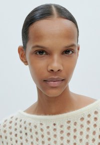 Leichter, gestrickter Pullover mit einem offenen Netzdesign und weitem Ausschnitt. Das Model hat glatte Haut und durchgestylte, nach hinten gekämmte Haare.