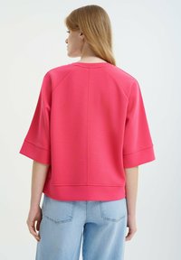 Short-sleeved, pink sweatshirt with a relaxed fit, featuring a round neckline and ribbed detailing. Material appears soft and textured.