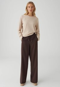 Beige top met lange mouwen en een ronde hals, gecombineerd met donkerbruine, wijde broek met verstelbare taille met trekkoord en zijzakken.