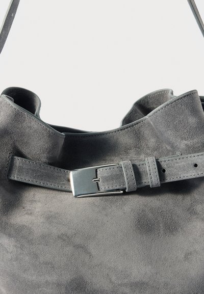 Sac à main en daim gris avec un haut roulé, doté d'une sangle de ceinture réglable grise et d'une boucle métallique. Texture douce et design minimaliste.