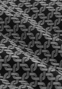 Black fabric featuring a woven pattern of interlocking silver lines, creating a textured and intricate design. Suitable for various textile applications.