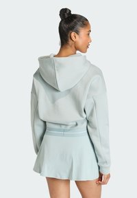 Svetlomodrá skrátená mikina s veľkou kapucňou, skombinovaná s rozšírenou svetlomodrou sukňou s páskovým akcentom. Hladká textúra látky.