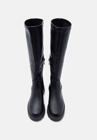 Ζευγάρι ψηλών μαύρων δερμάτινων μποτών με χοντρές σόλες και φερμουάρ στο πλάι, από πάνω σε λευκό φόντο.