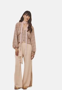 Blusa con un patrón de cuadros en rosa claro y marrón, combinada con pantalones de pierna ancha beige con aberturas laterales y acentos de borlas.