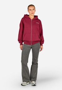 Burgundiška užtraukiama džemperis, pagamintas iš flisinės medžiagos, su priekinėmis kišenėmis ir žodžiu "PEGADOR", išsiuvinėtu ant kairiojo krūtinės.