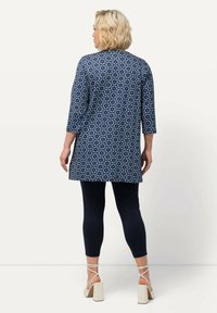 Tunique marine à motif floral et manches trois quarts, associée à des leggings marins et des sandales à talons carrés de couleur claire.
