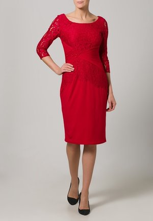 Robe rouge avec des manches en dentelle trois quarts, corsage ajusté et détail de taille froncée. Le tissu lisse contraste avec le revêtement en dentelle texturée.