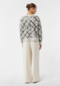 Sweter z dzianiny w jasnoszarym kolorze z ciemnym wzorem geometrycznym, noszony z szerokimi, kremowymi spodniami, prezentujący miękką teksturę i luźny krój.
