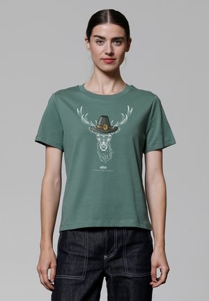 T-shirt en coton vert avec un graphisme représentant un cerf portant un chapeau, à manches courtes et à coupe décontractée. Notable par son ourlet droit et son col rond.