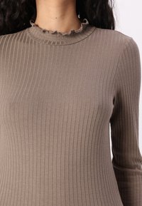 Brown ribbed long-sleeve top with a fitted shape and a frilled neckline detail, made from a soft, stretchy fabric.