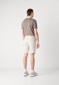 Kortermet, lys brun t-skjorte med rund hals, sammen med kremfargede cargo-shorts som har sidelommer og elastisk midjebånd.
