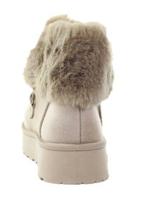 Beżowy botek za kostkę wykonany z zamszu z kołnierzem z futerka, zaokrąglonym kształtem, płaską gumową podeszwą i ozdobnym guzikiem po boku.