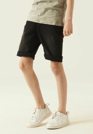 Sorte denimshorts med opkrogede kanter og slidte detaljer. Kombineret med hvide sportssko. Bomuldsstof, afslappet design.