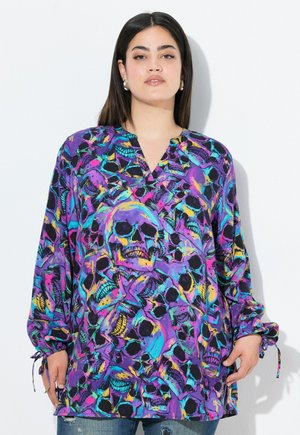 Blusa de manga larga con un fondo púrpura y un estampado vibrante de calaveras. La tela tiene una textura suave y cuenta con puños ajustables atados.