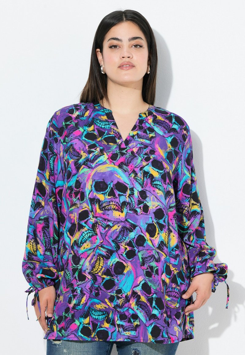 Langärmlige Bluse mit lila Hintergrund und einem bunten Totenkopf-Print. Der Stoff hat eine glatte Textur und verstellbare Krawattenmanschetten.