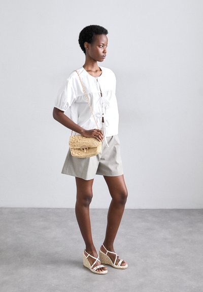Vit blus med puffärmar och knytning, grå shorts, halm crossover-väska och beige espadrillos med ankelremmar. Minimalistisk design.