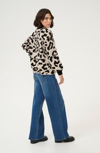 Maglione a stampa leopardata beige e nero con polsini a costine, abbinato a jeans blu a gamba larga a vita alta e stivali platform neri.