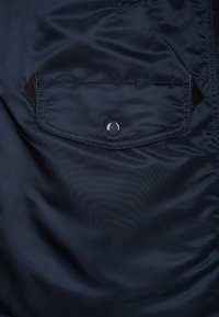 Navy blue fabric with smooth texture. Features a patch pocket secured by a snap button, outlined with black fabric accents.