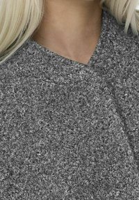 Tejido gris texturizado con una superficie suave y rizada, con un escote en forma de V y elementos de diseño superpuestos.