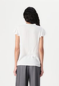 Haut blanc à manches courtes avec un tissu texturé, de subtils plis et un col, assorti à un pantalon gris ample.