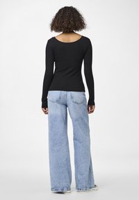 Black ribbed long-sleeve top with a wide neckline, paired with light blue wide-leg jeans, showcasing a relaxed fit and minimal stitching.