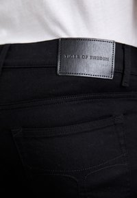 Svarta slim fit-jeans med en läderetikett i midjan, har bakfickor och subtila sömnadsdetaljer. Slät tygtextur.
