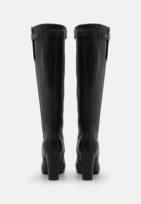 Black knee-high boots made from smooth leather, featuring a block heel, adjustable straps with gold accents, and a fitted shape.