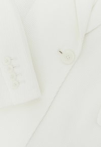 White textured blazer with four small buttons on the sleeve and one large button near the lapel, highlighting fabric detail.