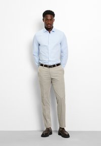 Camicia azzurro chiaro con bottoni, pantaloni beige chiaro, cintura marrone scuro e scarpe marroni. Vestibilità aderente con tessuto liscio e design strutturato.