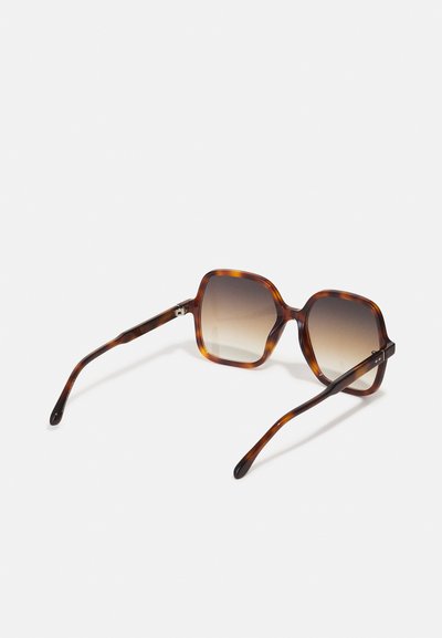 Lunettes de soleil carrées écaille de tortue avec verres marron dégradés reposant sur une surface blanche.