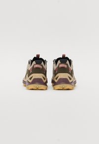 Tan- und olivfarbene Wanderschuhe mit schwarzen Akzenten, geformten Gummisohlen und roten Details. Verfügt über ein strukturiertes Obermaterial und eine ausgeprägte Ferse.