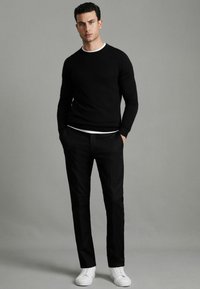 Pulover negru cu guler rotund, pantaloni negri și adidași albi. Textură tricotată pe pulover, pantaloni slim-fit, pantofi albi clasici. Stil simplu și modern.