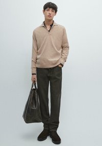 Maglione beige chiaro con scollo a V e polsini scuri a contrasto, abbinato a pantaloni verde scuro e una borsa tote in pelle marrone scuro.