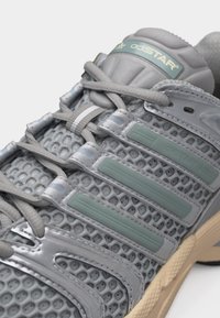 Εγγύς πλάνο γκρι αθλητικού παπουτσιού με δίχτυ επάνω, γκρι κορδόνια, ρίγες μέντας και μπεζ υφή στη σόλα.