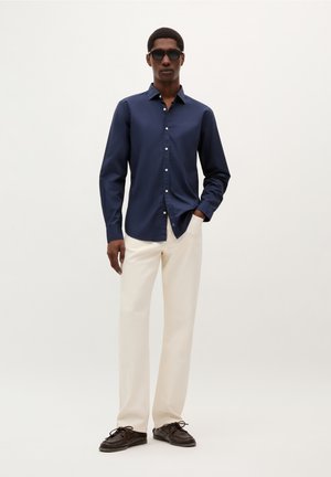 Navy button-up shirt with long sleeves, paired with cream-colored trousers and dark brown shoes, featuring a smooth texture and classic fit.