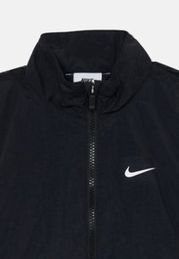 Nike svart zip-up jakke med høy krage, strukturert stoff, midt glidelås, og hvit logo aksent på venstre side.